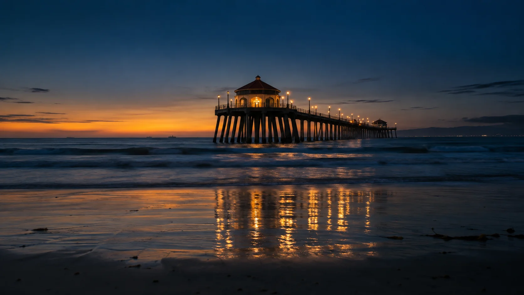 Huntington Beach Pier and empty beach at blue hour under a navy sky with an amber horizon